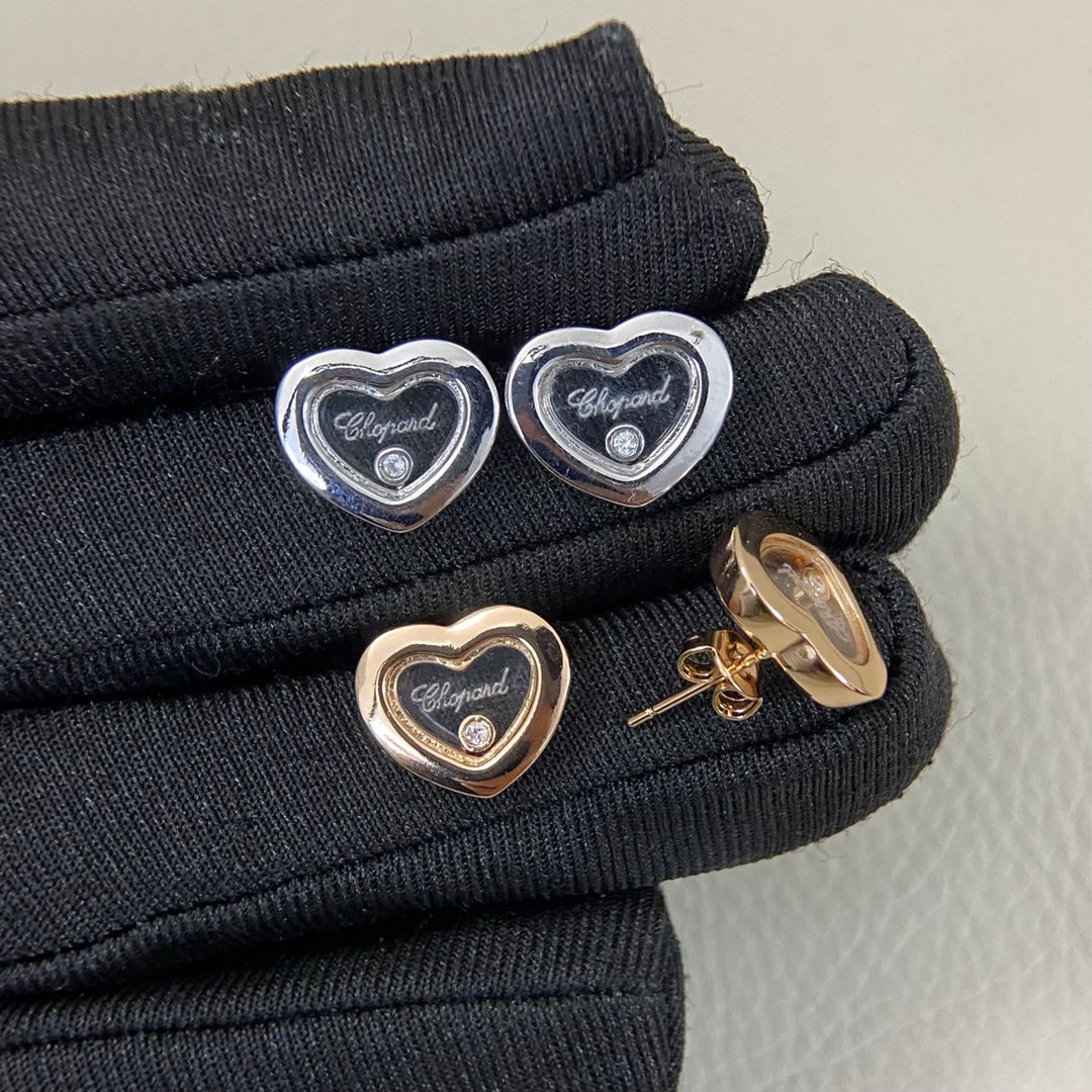 Heart stud earrings with single diamond; back clasp visible on black fabric