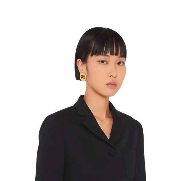 Round metal stud earrings with miu miu logo on model’s ear