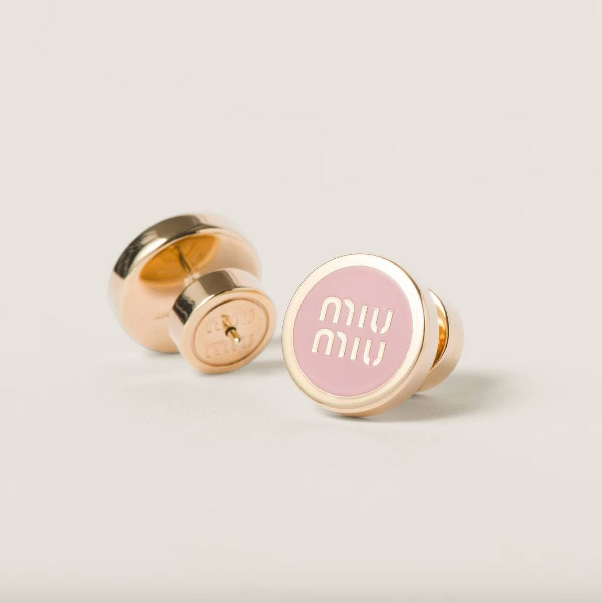 Gold-plated round enamel stud earrings with pink center and white 'miu miu' logo.