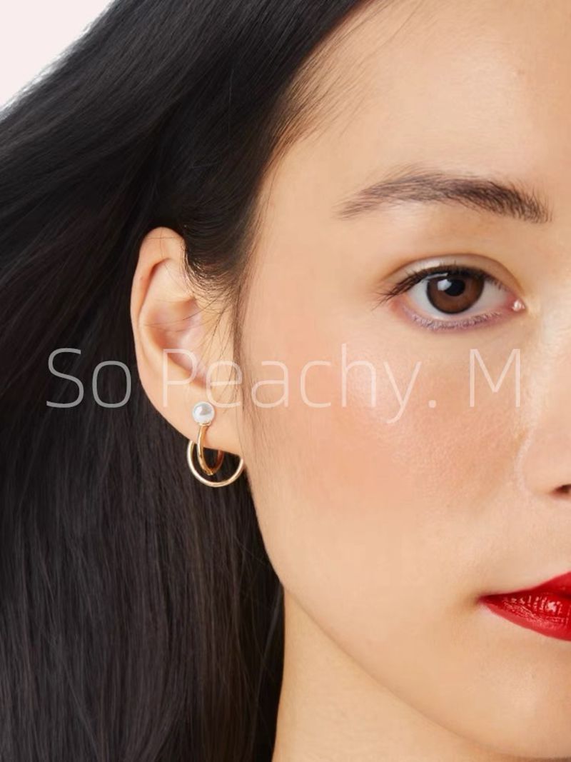 Gold-tone asymmetrical hoop earrings with pearl detail worn on ear