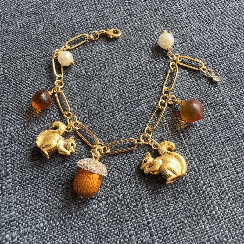 Gold-tone charm bracelet with squirrel, acorn, pinecone and pearl accents, chain links