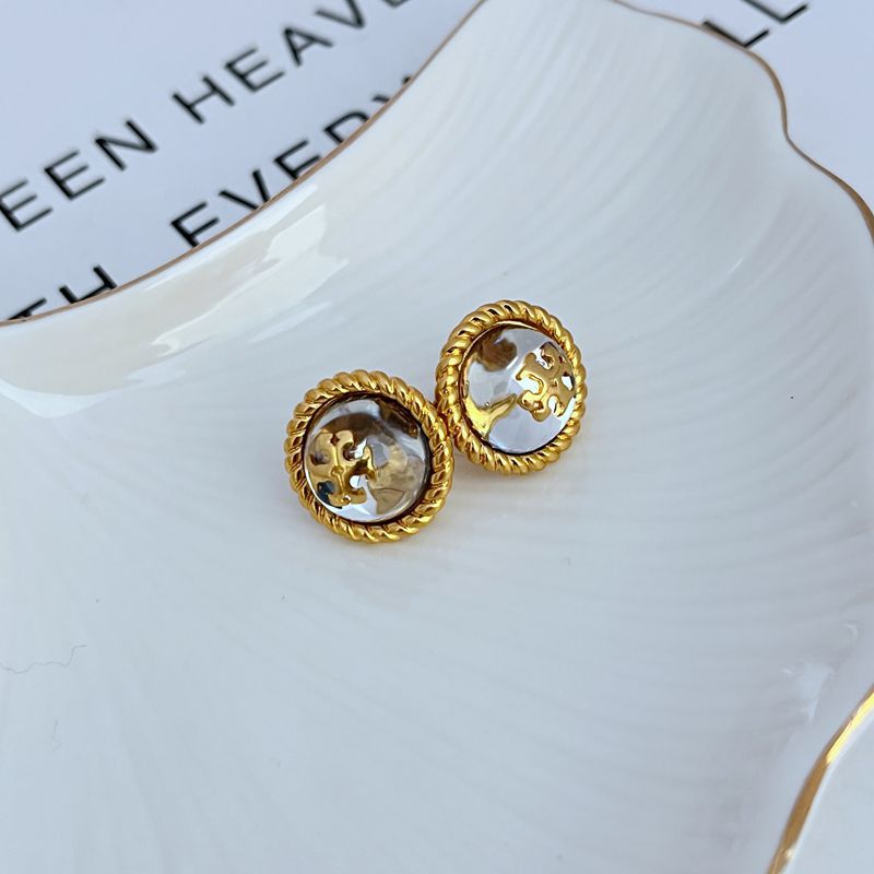 Round stud earrings, gold-tone bezel with clear/white resin faces and sculpted logo