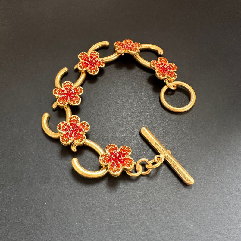 Rotes Blumenarmband mit goldfarbenen Gliedern und funkelnden Steinen, plus T-Knopf
