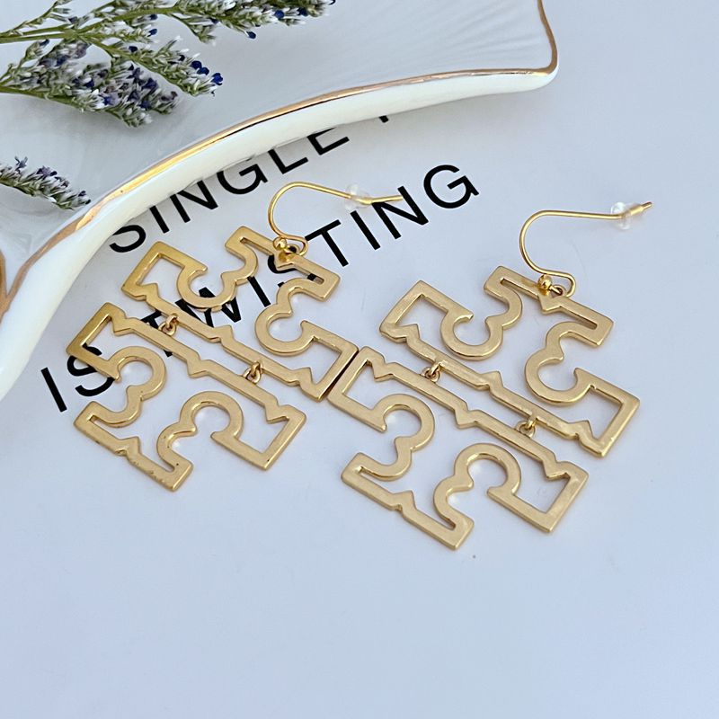 Gold metal openwork logo dangle earrings with hook backs, large square cutout frames.