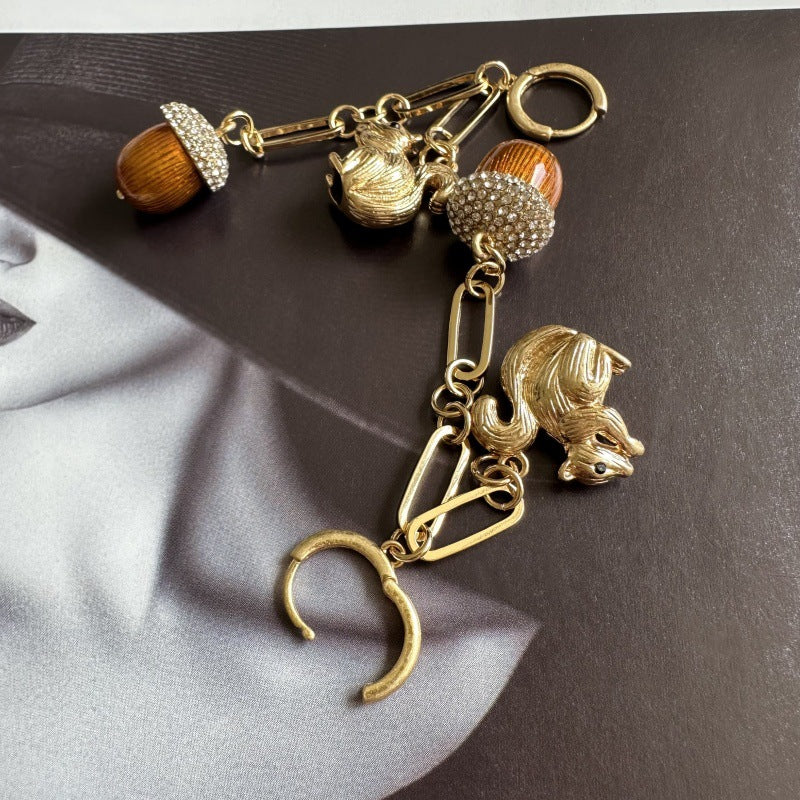 Gold drop earrings with squirrel charm, pinecone accent, and long linked tassel drops