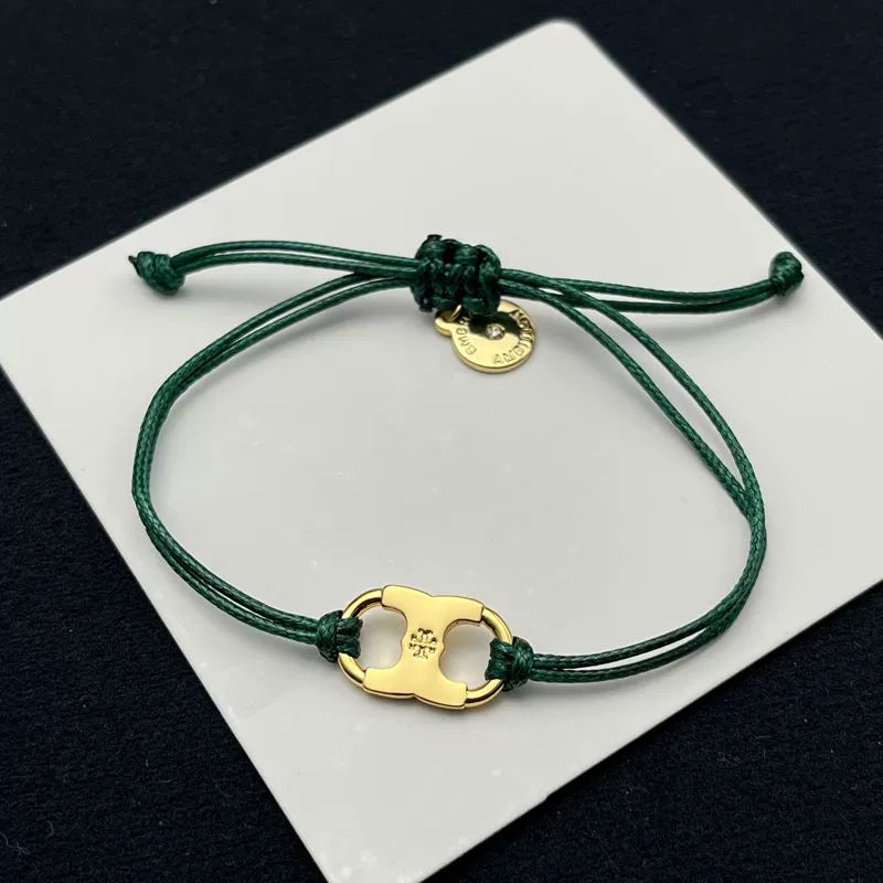 Green woven adjustable drawstring bracelet with gold clover enamel charm and small round tag