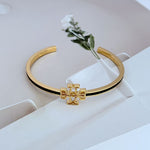 Gold open metal bangle with cutout logo and dark enamel trim