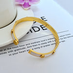 Goldfarbenes Metallarmband mit Logo-Emaille und seitlichen Kugelverzierungen