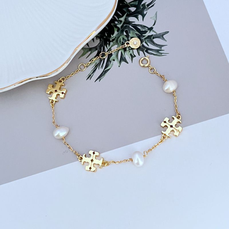 Gold-tone bracelet featuring round charm and pearl accents with puzzle-link details