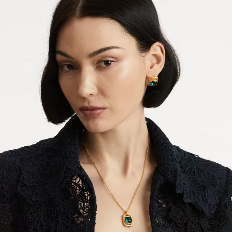 Gold-tone square pendant necklace with green gemstone, worn on model