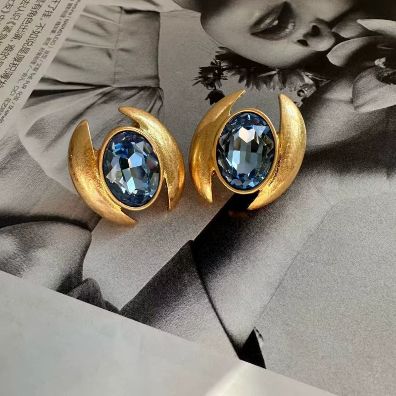 Dark blue oval crystal stud earrings with gold crescent prongs and oval bezel frame.