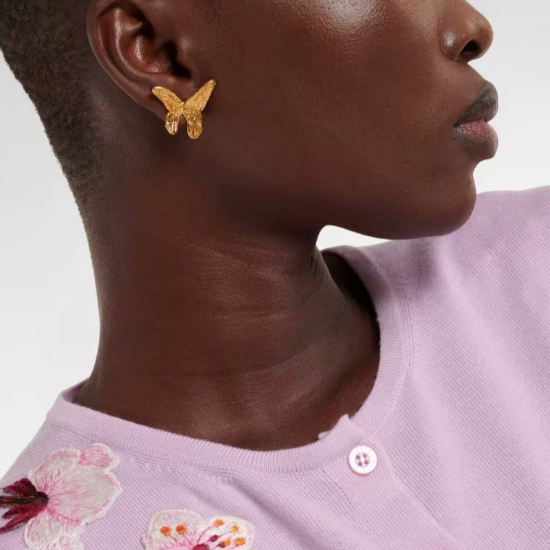 Gold butterfly earrings on ear, small textured wing charms.