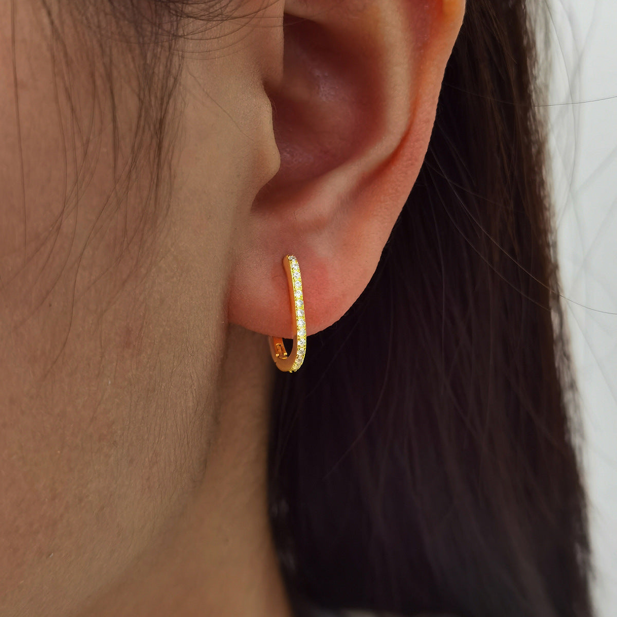 Gold zirconia U-shaped hoop earring worn on ear