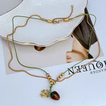 Gold double necklace with raspberry enamel pendant, bead stations, and green cords