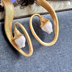Gold-tone clip-on earrings close-up: oval hoop with white bell flower charm