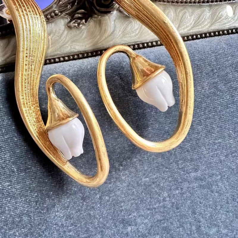 Gold-tone clip-on earrings close-up: oval hoop with white bell flower charm