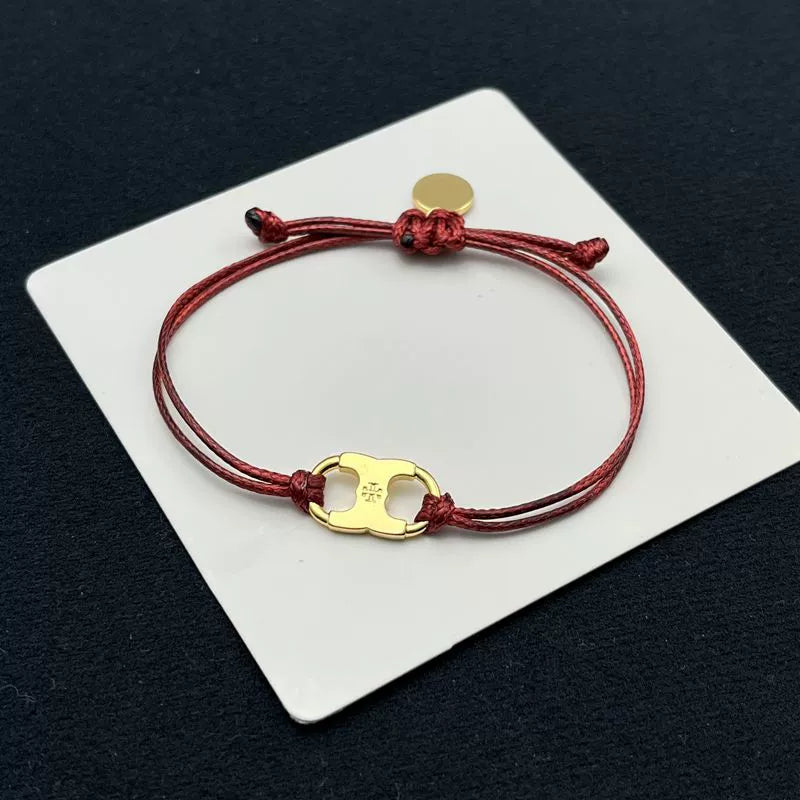 Red woven adjustable drawstring bracelet with gold clover enamel charm and round tag
