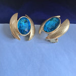 Light blue oval crystal stud earrings with gold curved halo and prong setting.