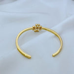 Gold open metal cuff bangle with square logo at top center