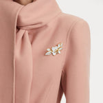 Small white enamel flower brooch with gold leaves and crystal center on fabric