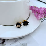 Black four-leaf clover stud earrings with gold-tone center detail
