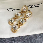 White crystal long drop earrings with three faceted stones in ornate gold-tone frames