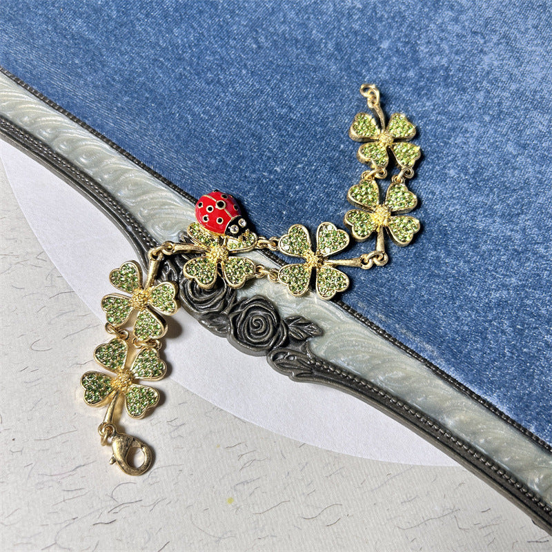 Gold-tone ladybug and four-leaf clover charm bracelet with dangling flower chain links