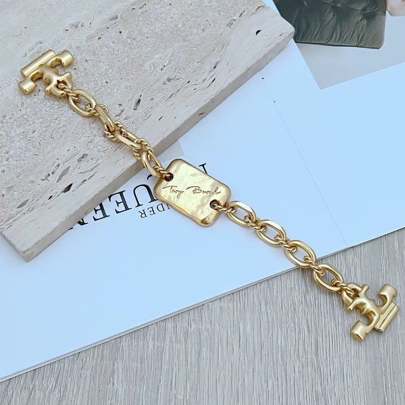 Gold chain bracelet/necklace close-up of engraved rectangular tag and H charm