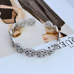 Silver-tone circular openwork logo bangle with diamond-studded oval links