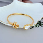 Gold open bangle showing mother-of-pearl heart charm and heart clasp centerpiece