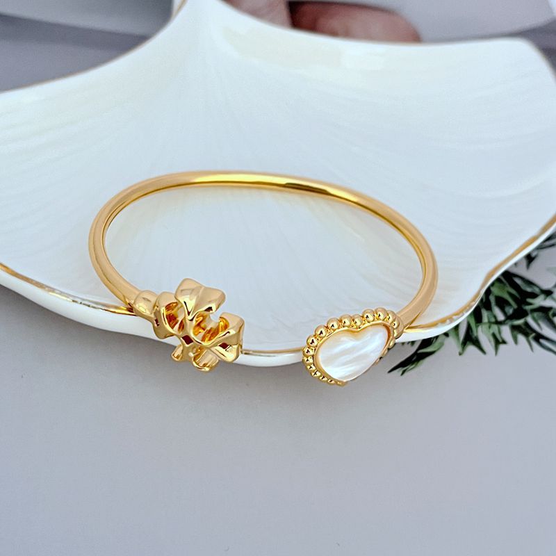 Gold open bangle with heart-shaped charm and mother-of-pearl oval detail