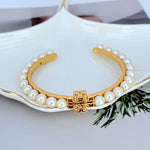 Pearl Logo open bangle: gold-tone cuff with white pearls and red-gold center clasp