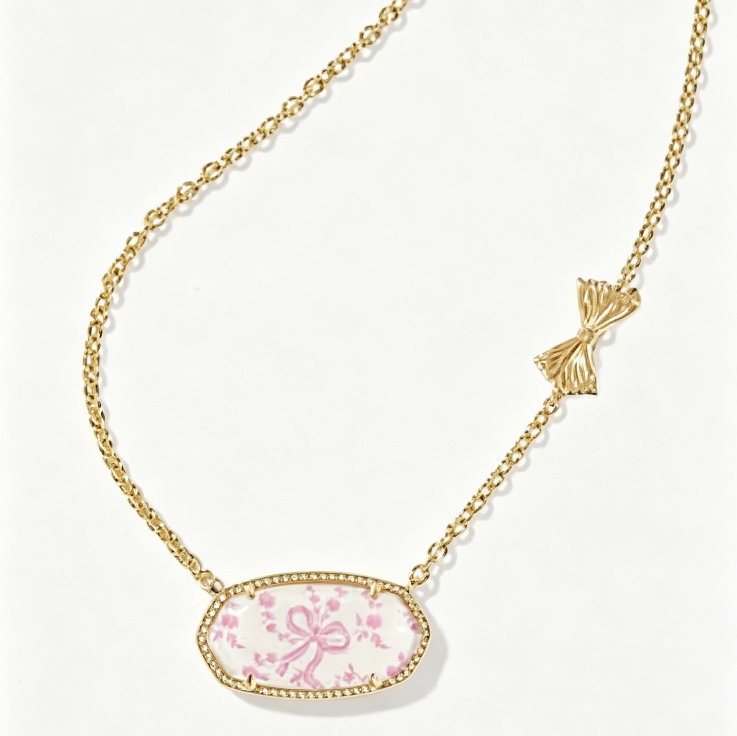 Gold-tone oval pendant necklace with pink floral cabochon and bow accent