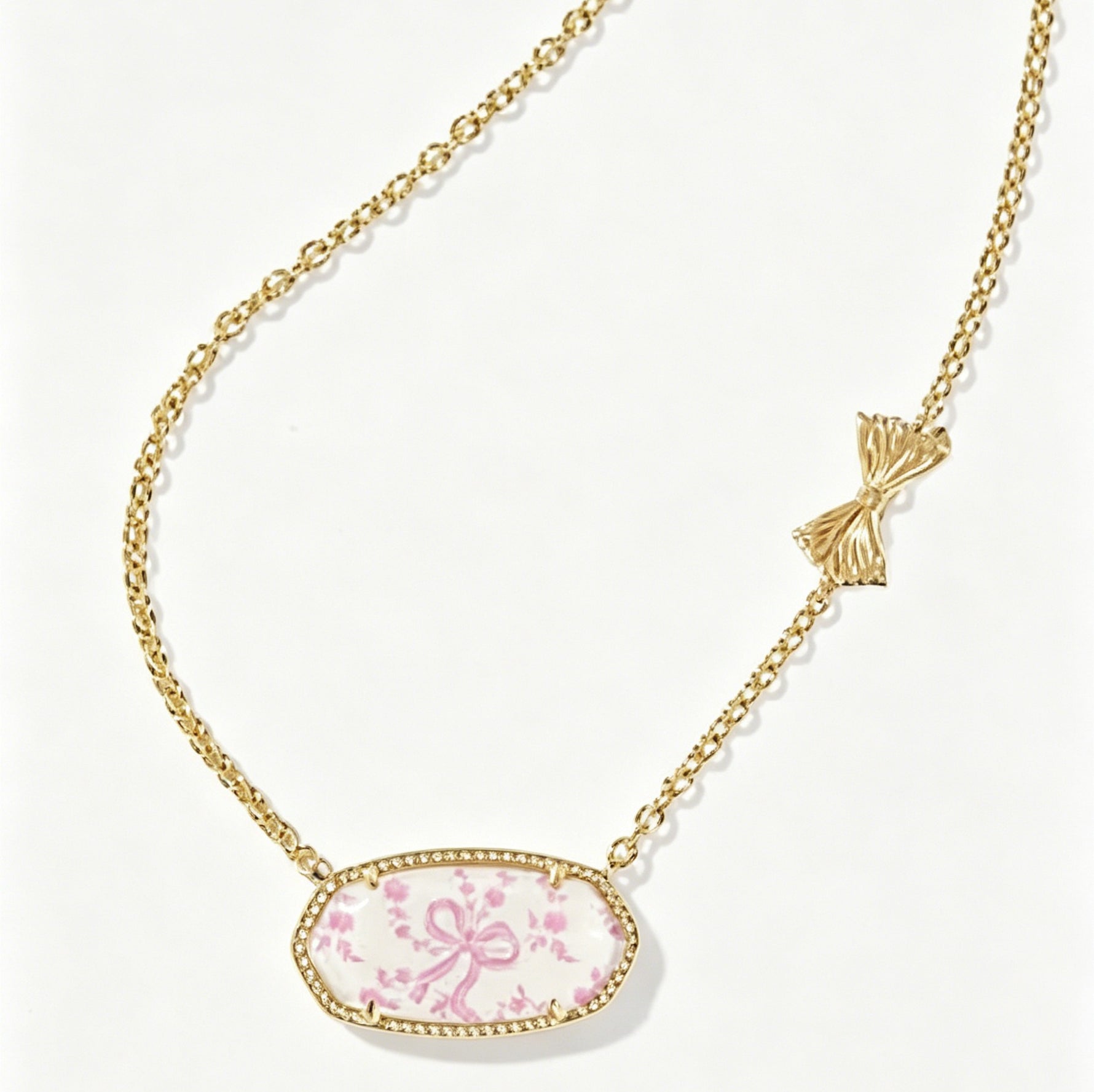 Gold-tone oval pendant necklace with pink floral cabochon and bow accent