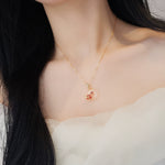 Gold-tone chain necklace with round white pendant featuring red flower enamel
