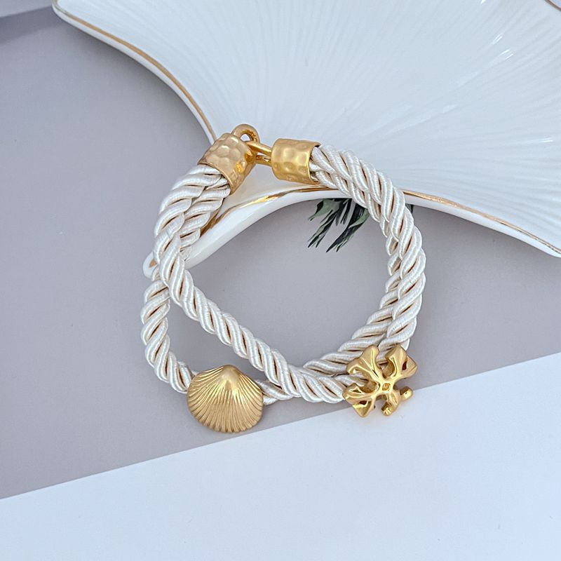 Braided cord bracelet with gold shell and logo charms, white cord with gold accents.