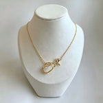 Gold-tone charm necklace on a mannequin with openwork heart pendant and dangling charm