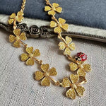 Gold four-leaf clover necklace with red ladybug accent and textured clover charms