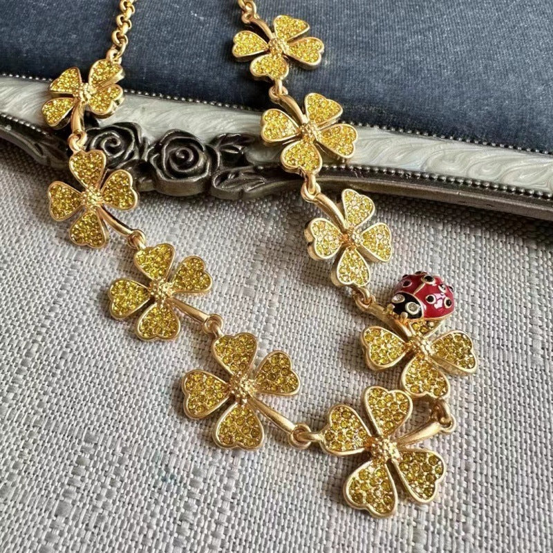 Gold four-leaf clover necklace with red ladybug accent and textured clover charms