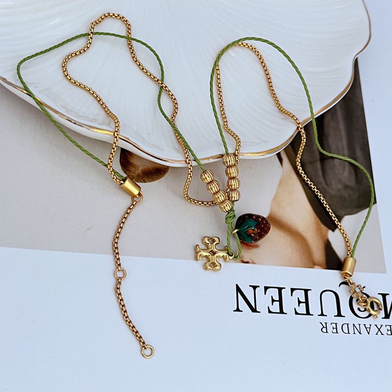 Gold-tone double necklace showing layered chains, green beaded drop and small cross charm