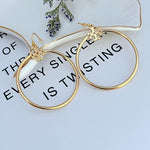 Large round gold hoop earrings with small quatrefoil charm