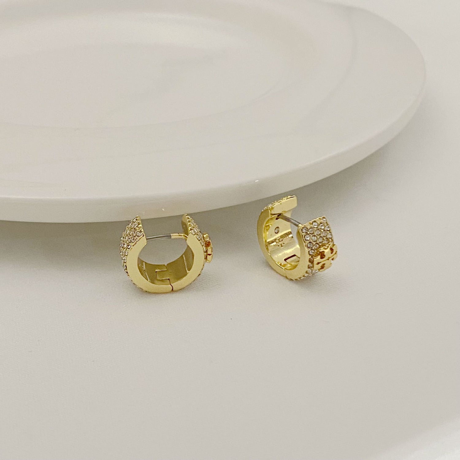 Gold-tone crystal logo hoop earrings, side view with hinged clasp