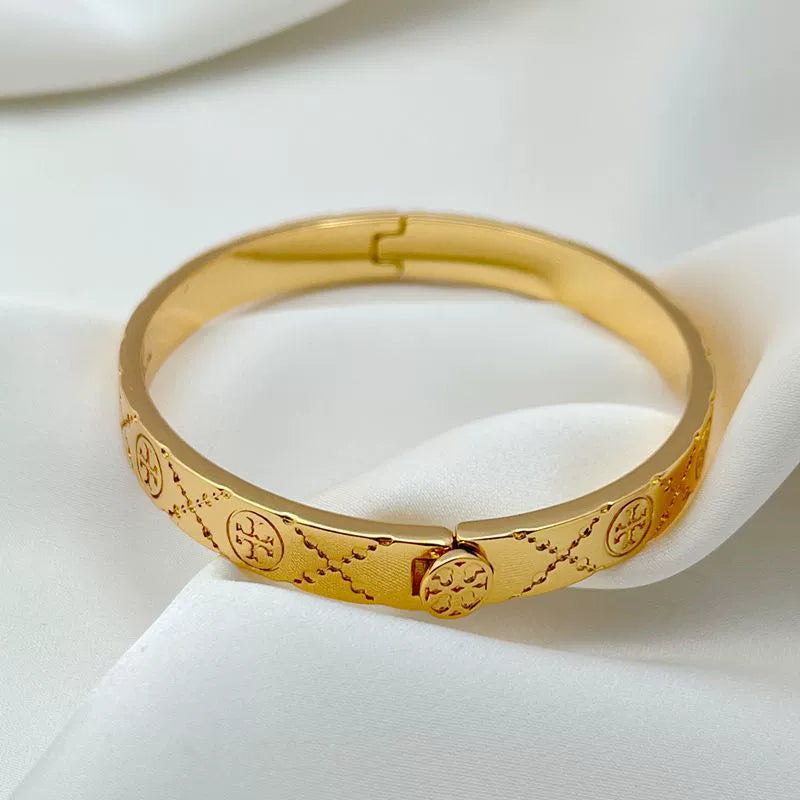 Gold hinged bracelet with central oval logo detail and textured pattern