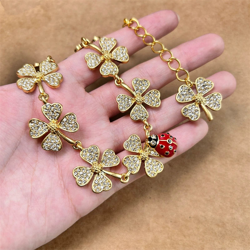 Four-leaf clover necklace with red ladybug charm and pavé-flower links, close-up