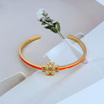 Gold open metal bangle with cutout logo and red enamel edge stripe