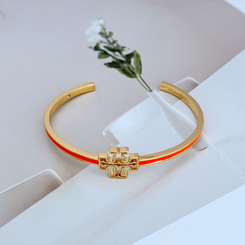 Gold open metal bangle with cutout logo and red enamel edge stripe