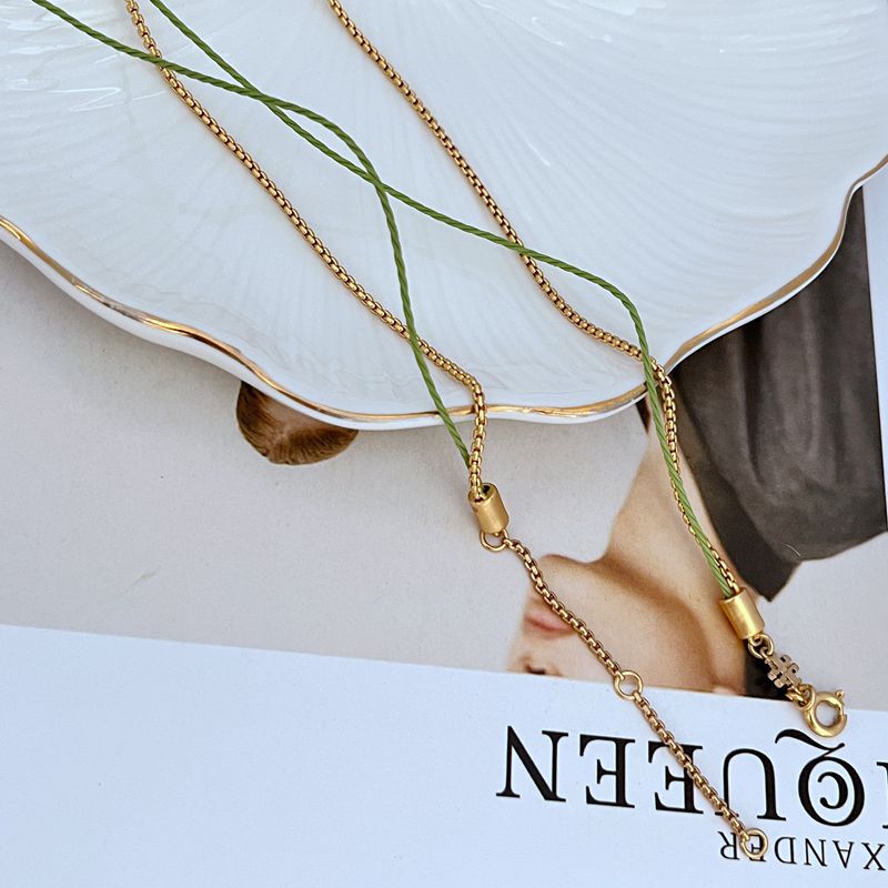 Gold double necklace with clasp, linked chain, green cords, and raspberry charm