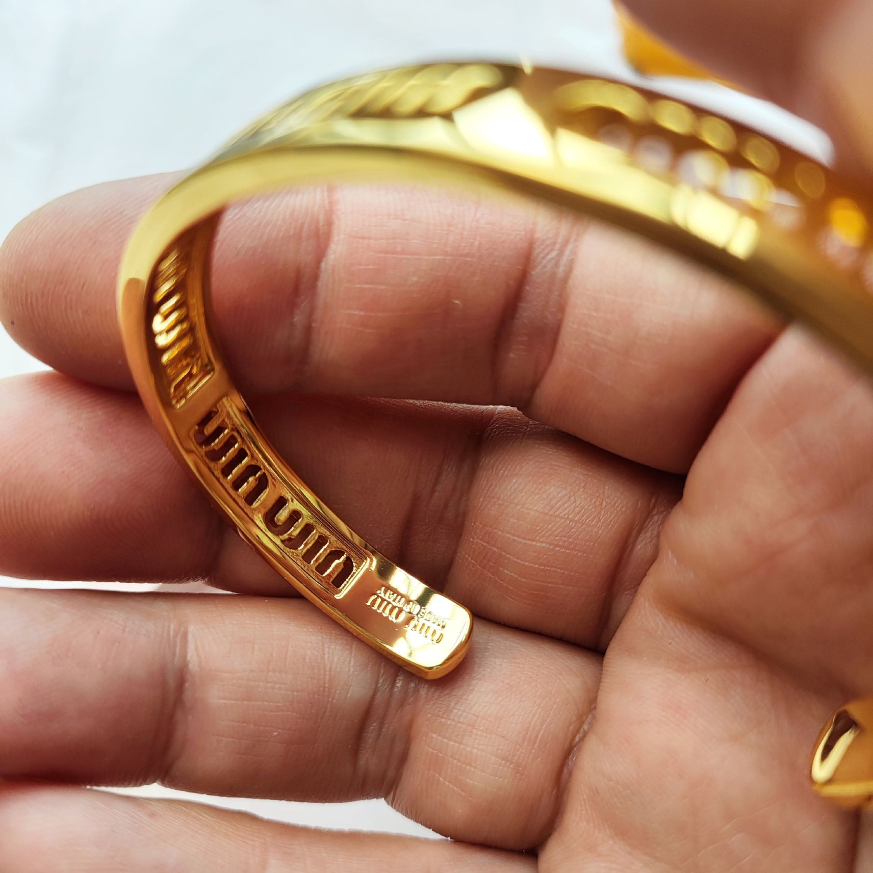 Gold openwork logo bangle close-up, engraved logo text along the open cuff edge