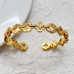 Gold tone four-leaf clover openwork bangle with central clover clasp and linked charms
