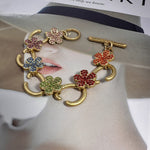 Buntes Blumenarmband mit goldfarbenen Gliedern und funkelnden Steinen in Plomme-Optik